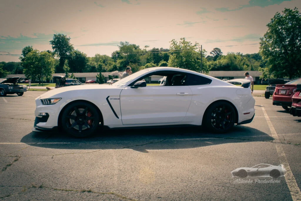 White Ford Mustang GT350 coupe parked in an outdoor lot during a daytime car event