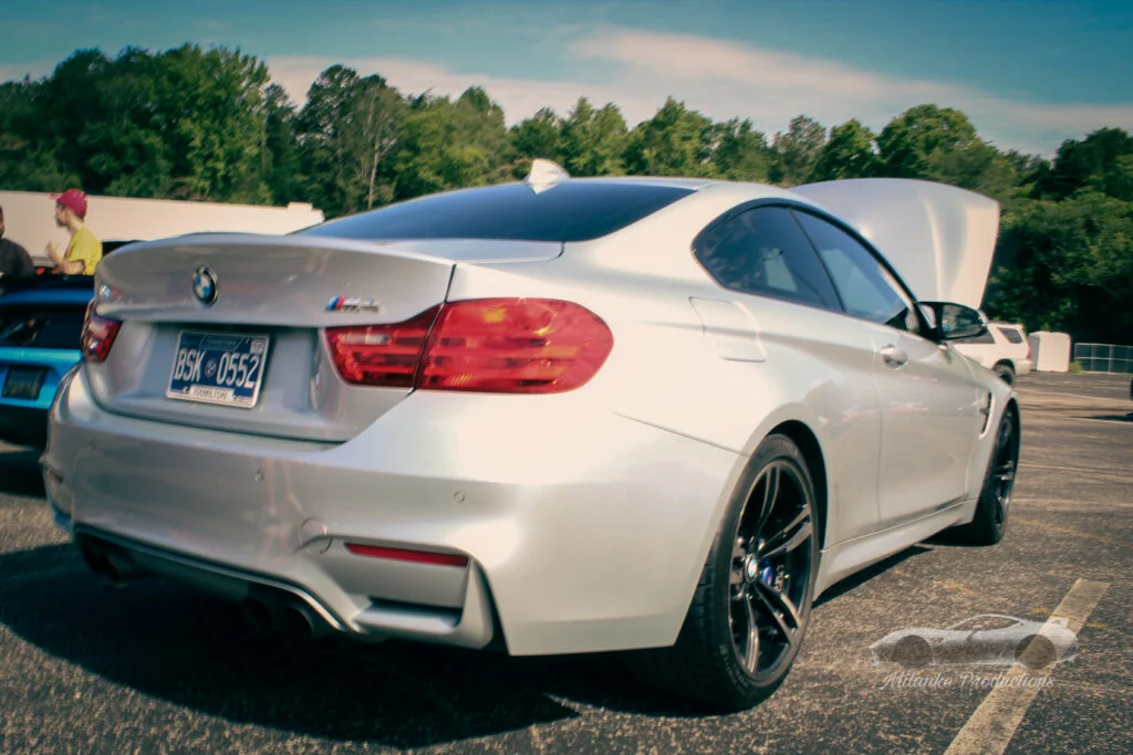 White BMW M4 with open hood parked outdoors with trees and people nearby