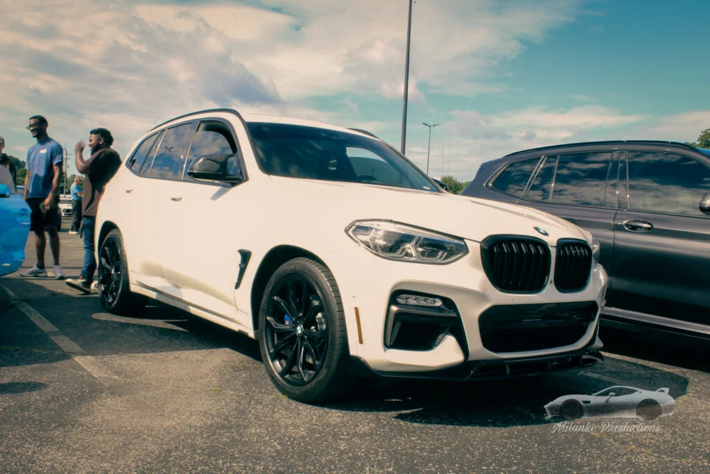 White BMW X3 parked in a lot with a group of people nearby under a partly cloudy sky.