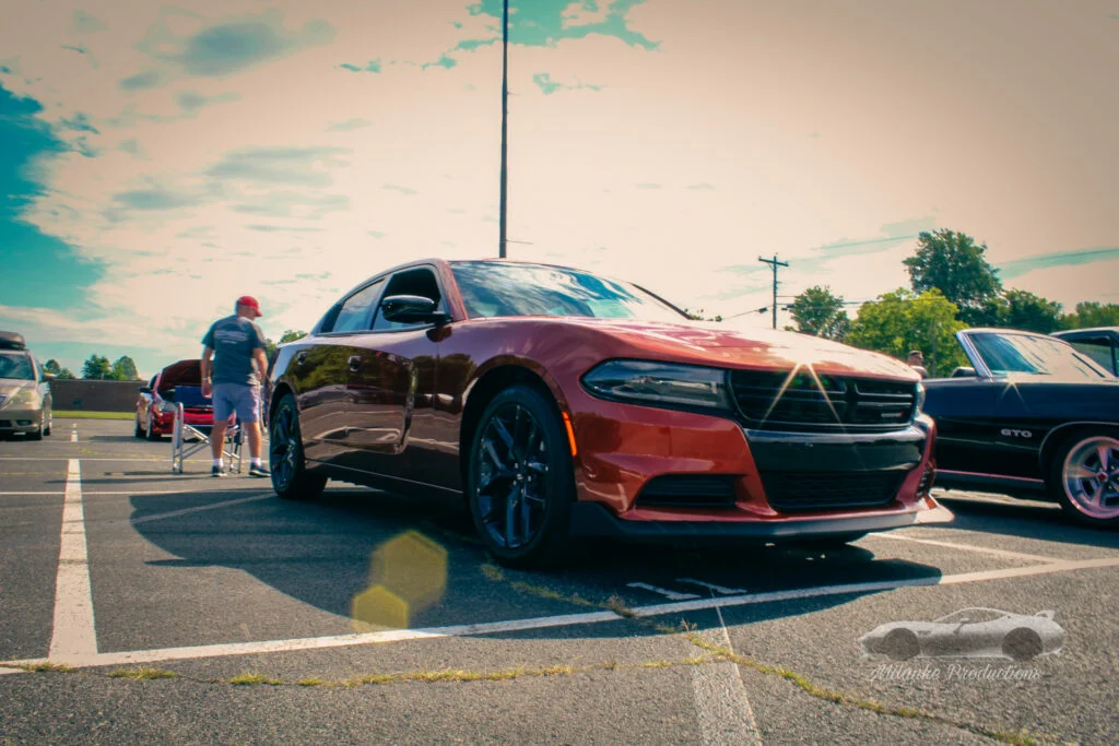 Red Dodge Charger parked in an outdoor car meet with other vehicles and people visible