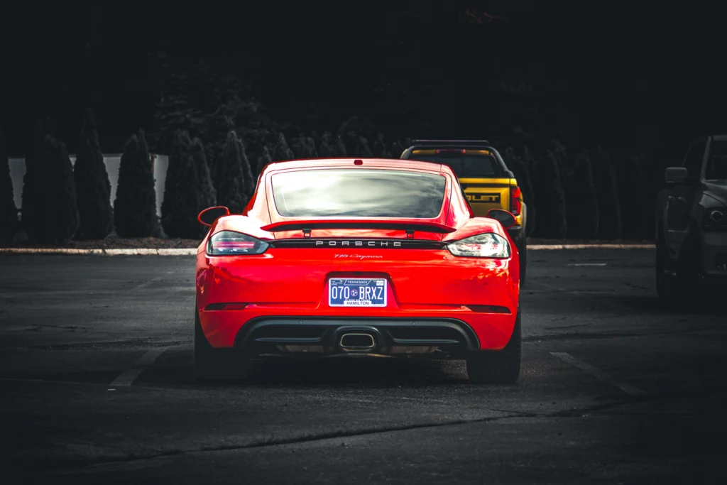 Red Porsche 718 Cayman parked with a yellow Chevrolet truck and a gray vehicle nearby