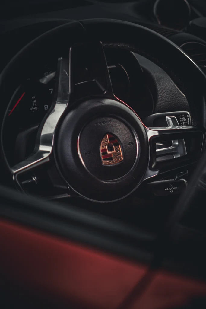 Close-up of a Porsche steering wheel with dashboard and red interior visible