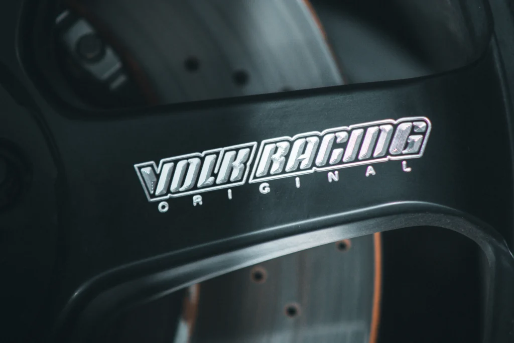 Close-up of black Volk Racing wheel center with logo and drilled brake rotor behind