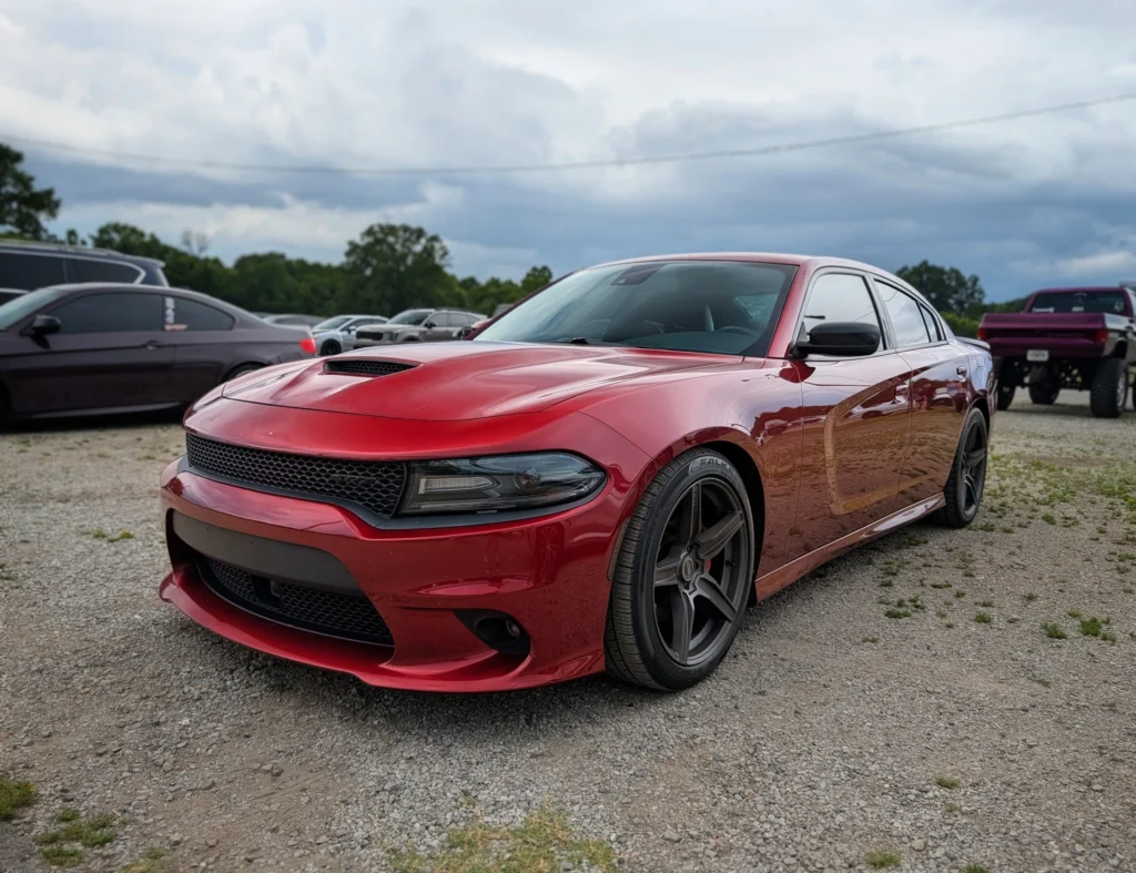 Red Dodge Charger sedan parked on gravel with several other vehicles in the background under a cloudy sky