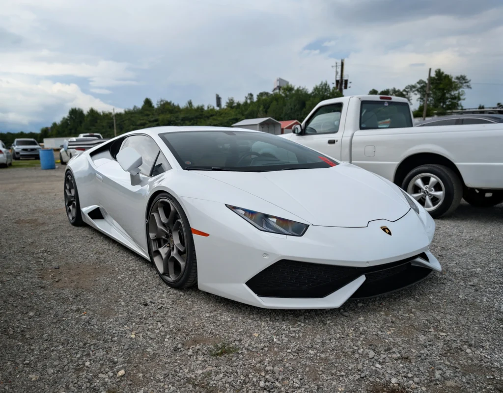 White Lamborghini Huracán parked on gravel with other vehicles in background under cloudy sky