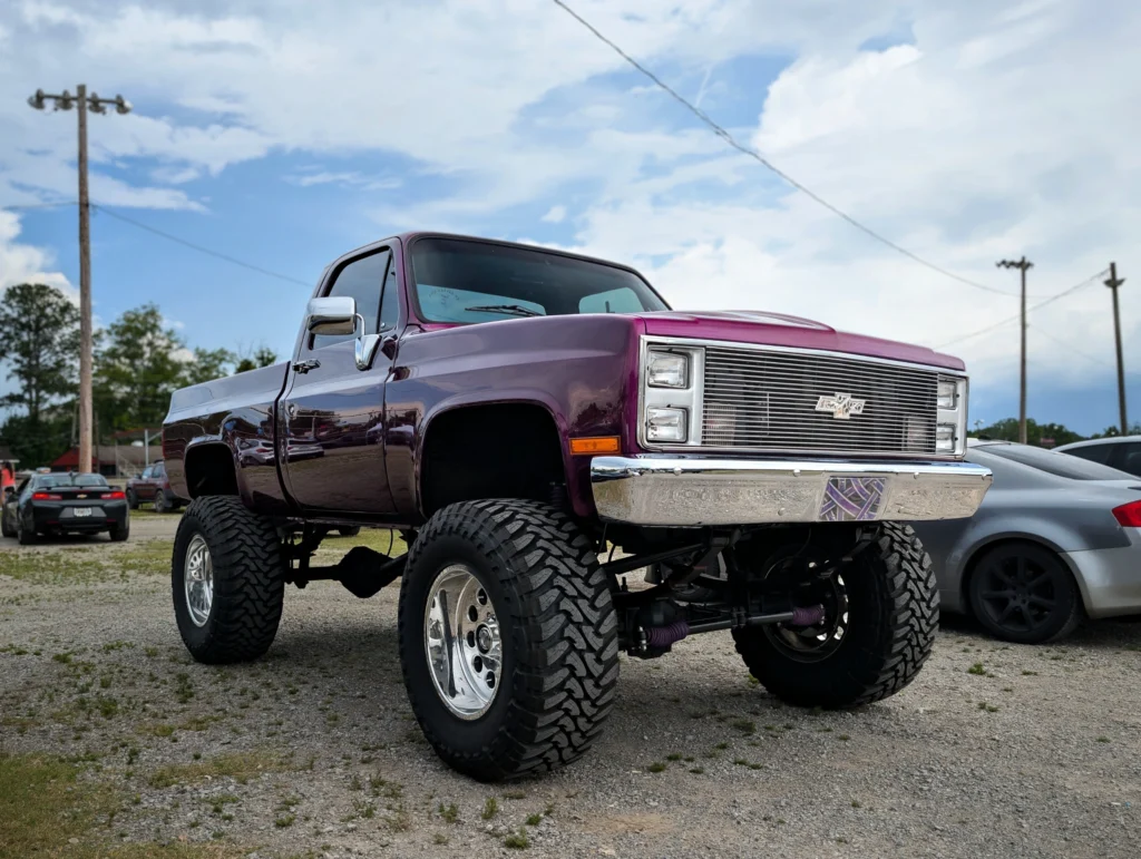 Purple lifted Chevrolet C/K parked outdoors under a blue sky with power lines and other cars in background