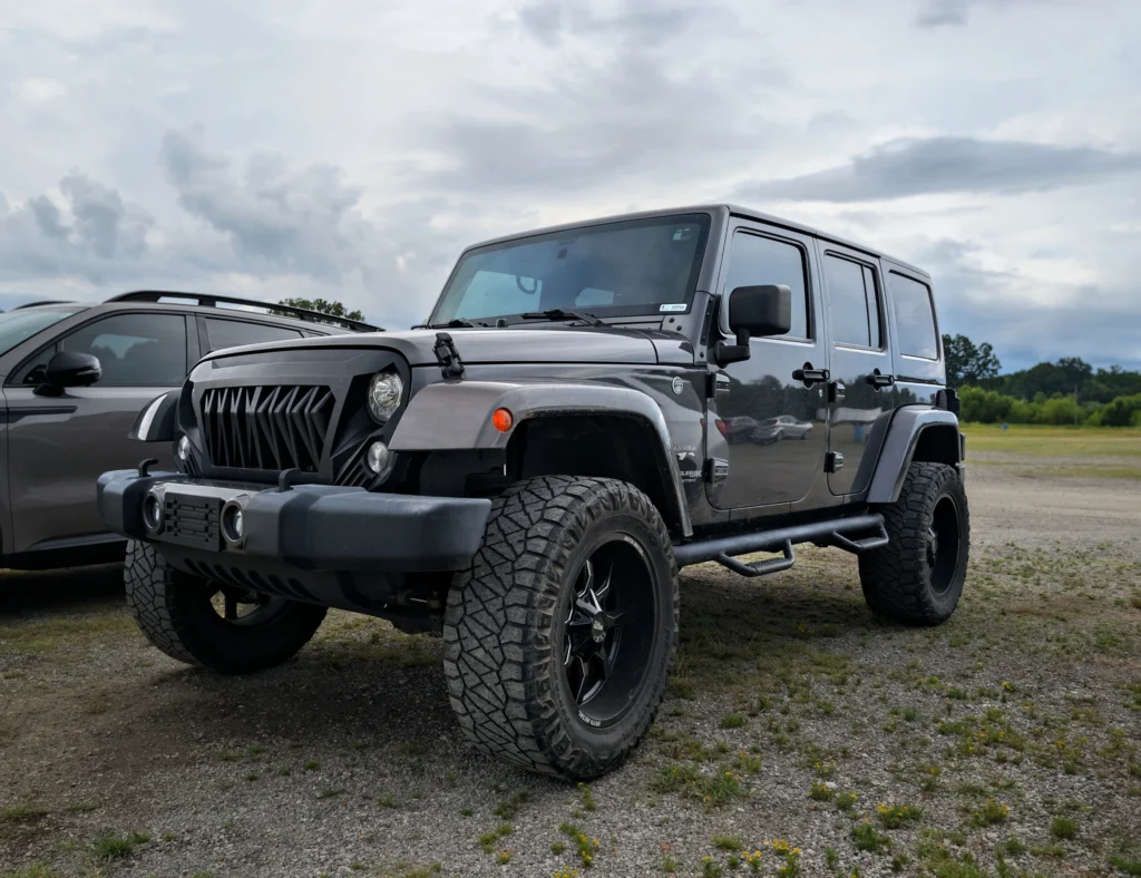 Black Jeep Wrangler Sahara four-door parked on gravel with cloudy sky background