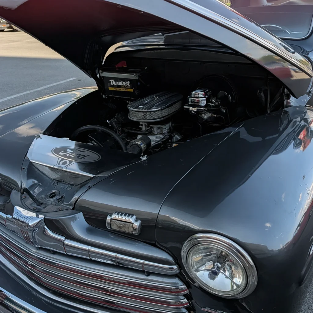 Open engine bay of a black vintage Ford vehicle showing a Duralast Gold battery and engine components