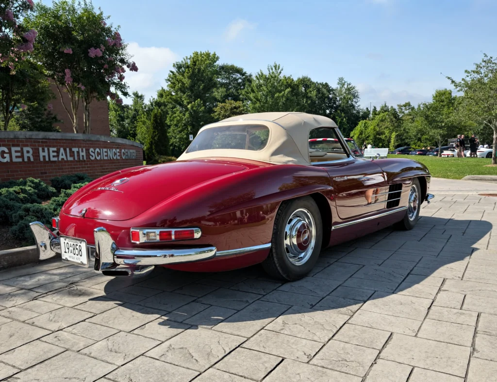 Red Mercedes-Benz 300SL convertible with beige soft top parked outside a health science center on a sunny day