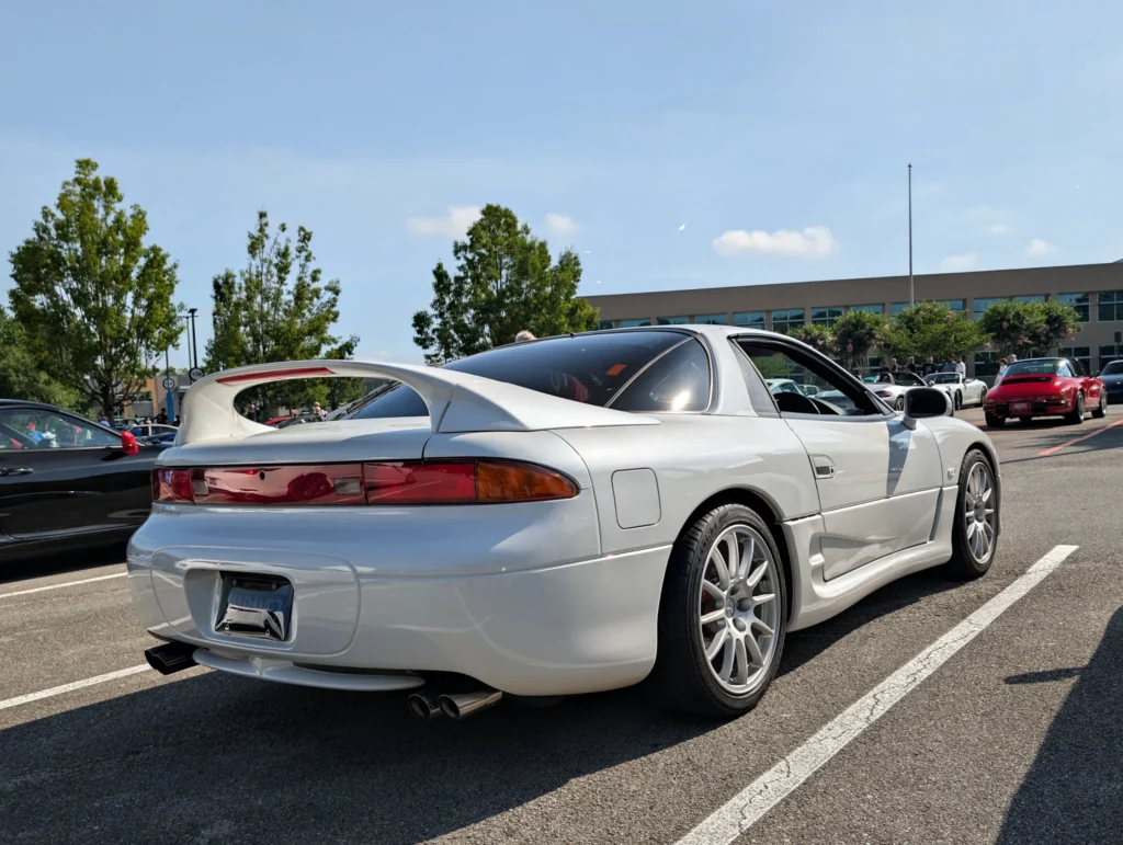 White Mitsubishi 3000GT parked with other cars and people in a sunny parking lot at a car event