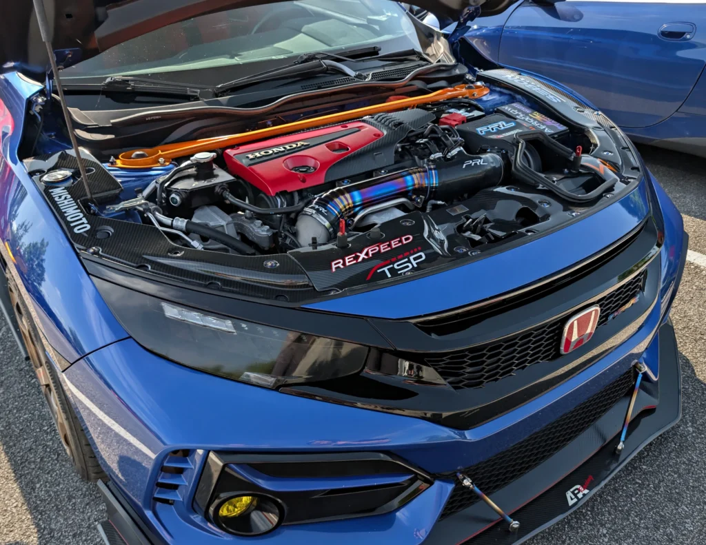 Open engine bay of a blue Honda Civic Type R with aftermarket parts and detailing, parked next to a blue car.