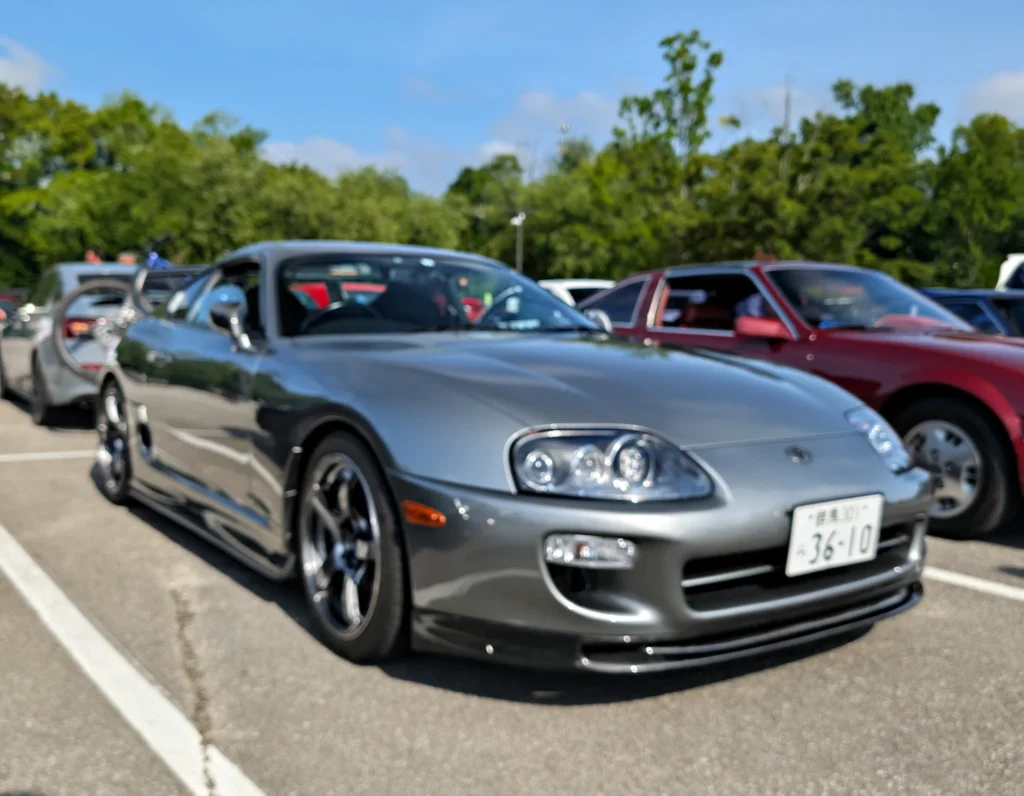 Silver Toyota Supra parked at a car event with other vehicles and trees in the background