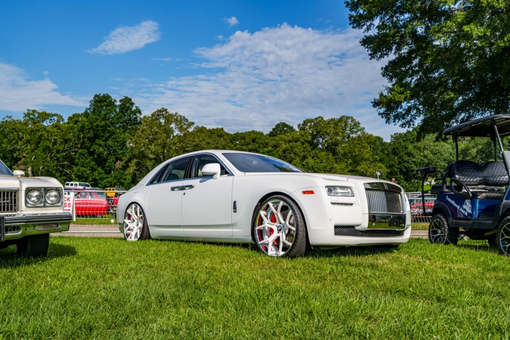 White Rolls-Royce sedan parked on grass at outdoor car event with other vehicles and trees in background
