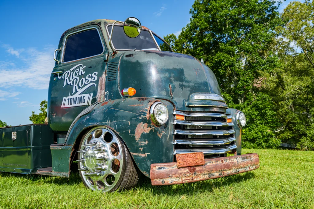 Green Chevrolet tow truck with rust spots parked on grass under blue sky