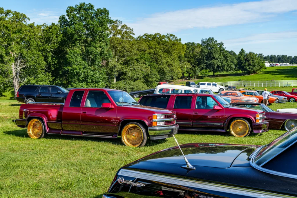 A maroon Chevrolet pickup, SUV, and a black Chevrolet Impala parked on grass at an outdoor car event