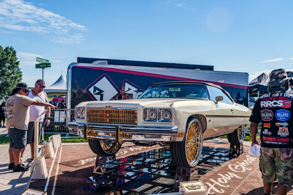 Ivory Chevrolet Caprice convertible on reflectors with gold wheels at outdoor car event