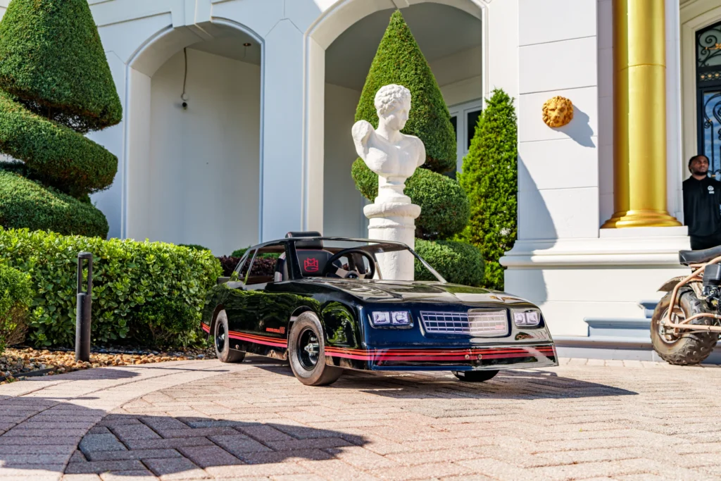 Black Chevy Monte Carlo SS pedal car parked in front of a building with white pillars and topiary trees