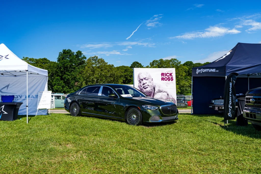 Black Mercedes-Maybach sedan parked on grass between white and blue tents at a car event under a clear sky