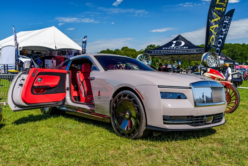 Silver Rolls-Royce with open Passenge side door showing red interior at an outdoor car event on grass with tents and wheels i
