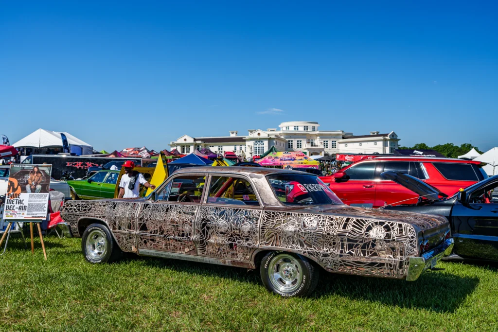 Metallic rusty-colored Chevrolet Bel Air with intricate metal cutout pattern parked on grass at car event