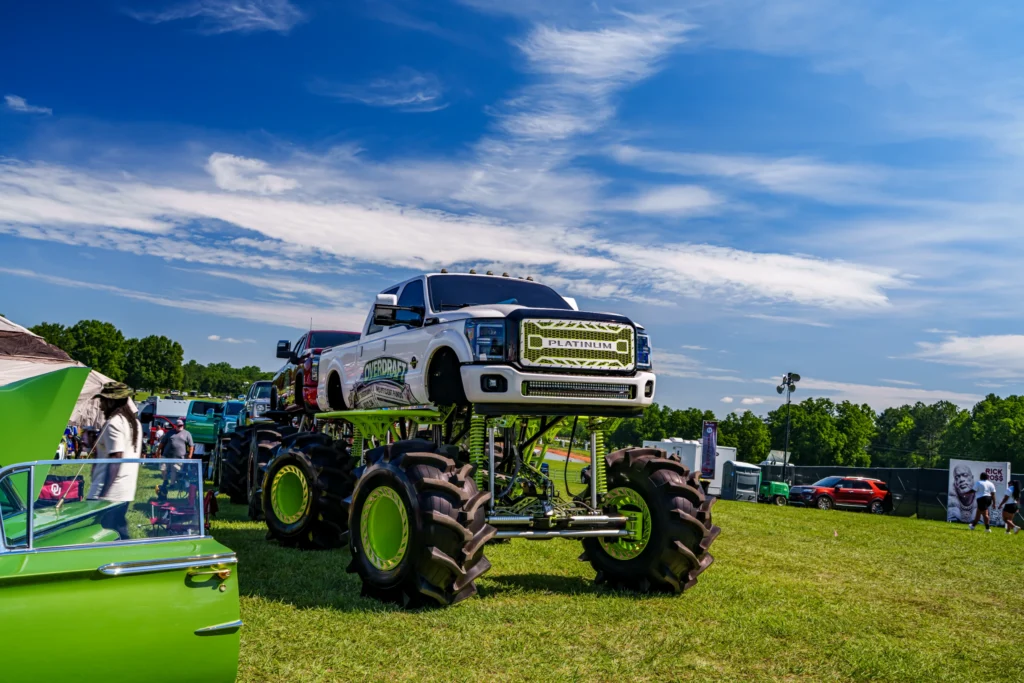 White Ford Platinum pickup truck lifted on large green and black monster truck wheels at outdoor car event