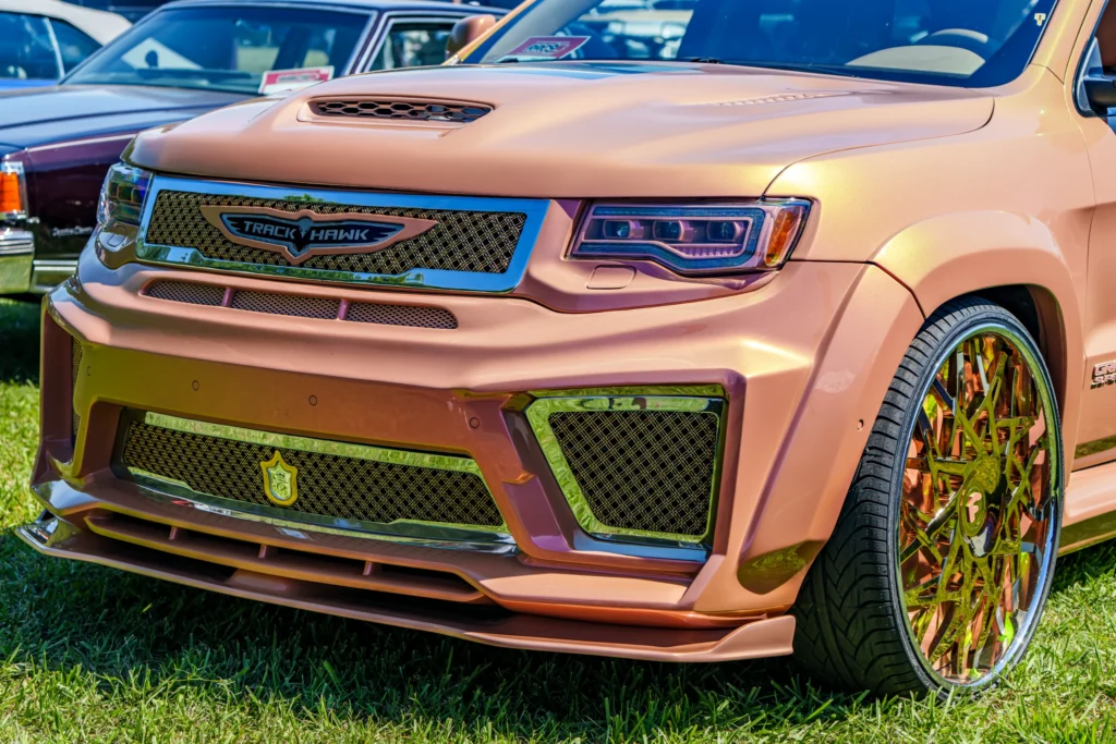 Gold Dodge Durango Trackhawk with custom grille and gold rims parked on grass at a car event