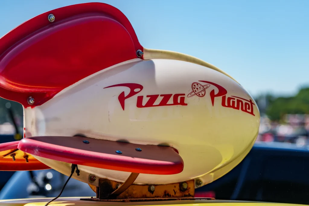 Red and white Pizza Planet rooftop sign mounted on a vehicle with blue sky background