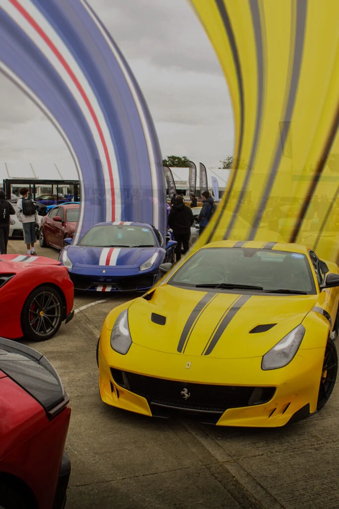 Yellow Ferrari with black racing stripes and blue Ferrari with white and red racing stripes parked outdoors with people and t