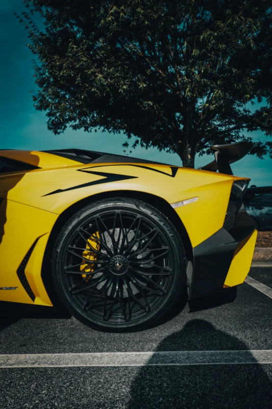 Yellow Lamborghini Aventador with black rims parked outdoors under a tree
