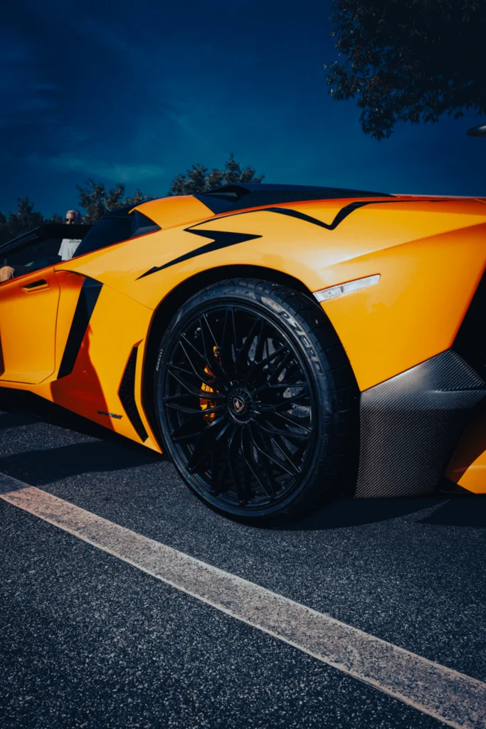 Close-up of the rear section of an orange Lamborghini with black wheel and black stripe detail under clear blue sky