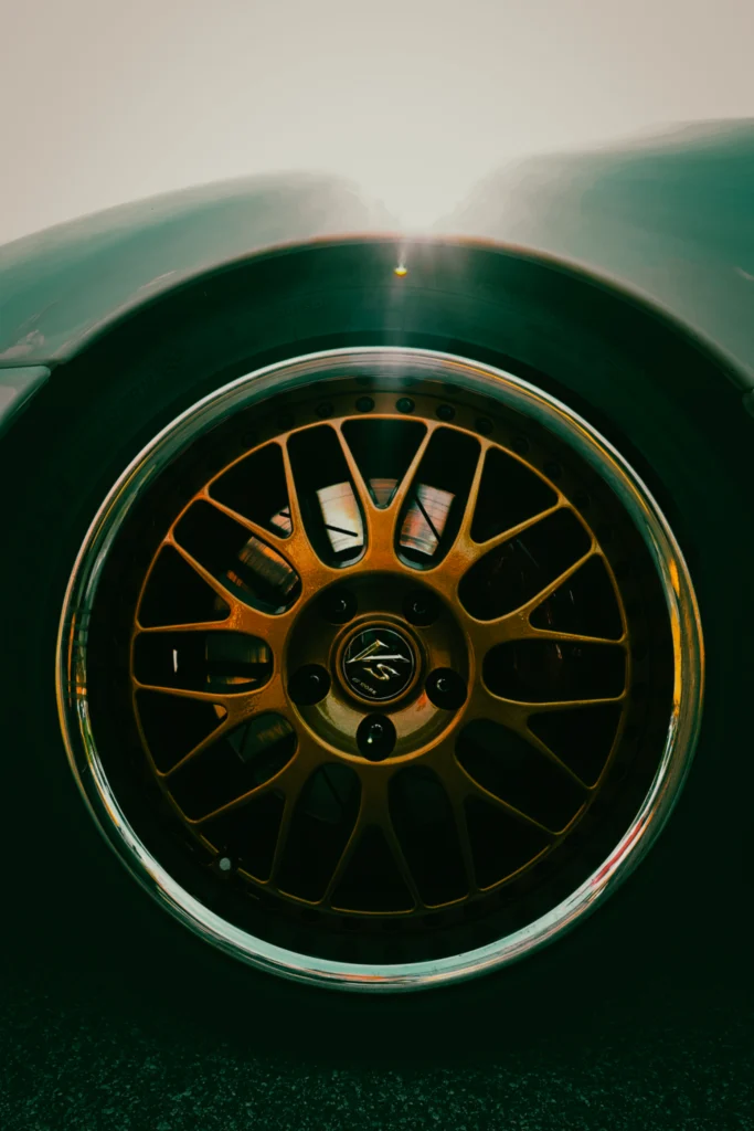Close-up of a gold multi-spoke wheel and tire on a teal vehicle with sunlight reflecting off the fender