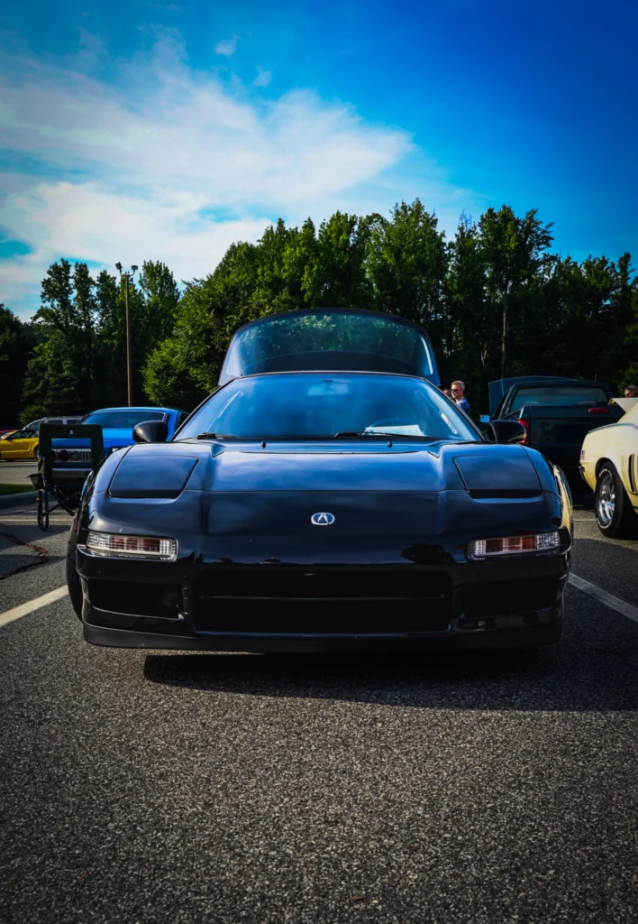 Black Acura NSX with hood open in a parking lot at a car event with trees and blue sky in the background