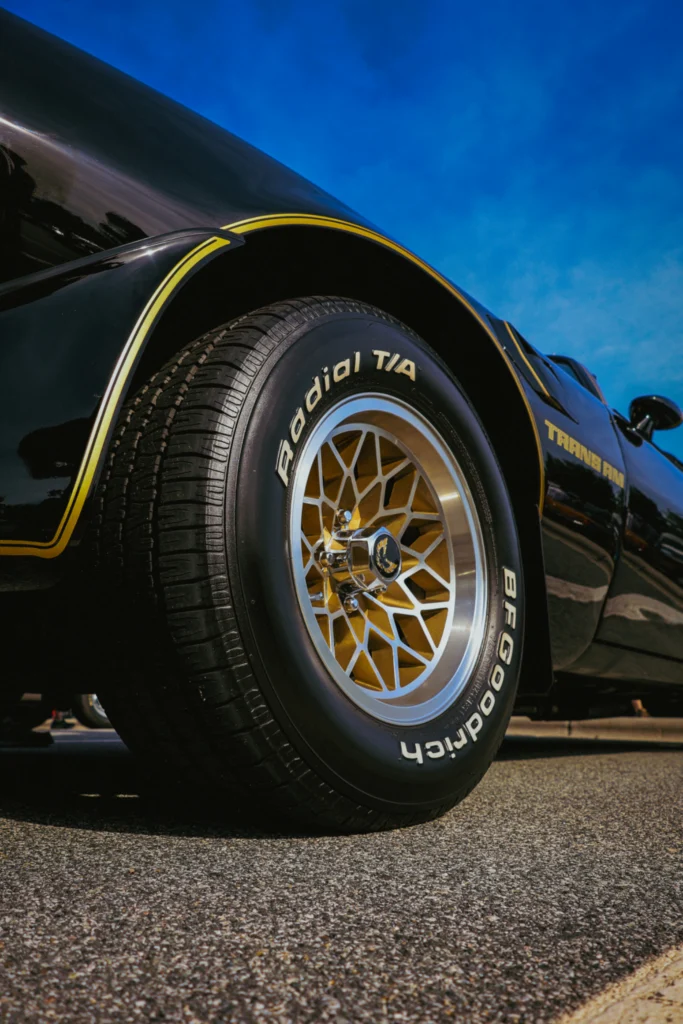 Black Pontiac Trans Am with gold trim and BFGoodrich Radial T/A tire on paved surface under clear blue sky