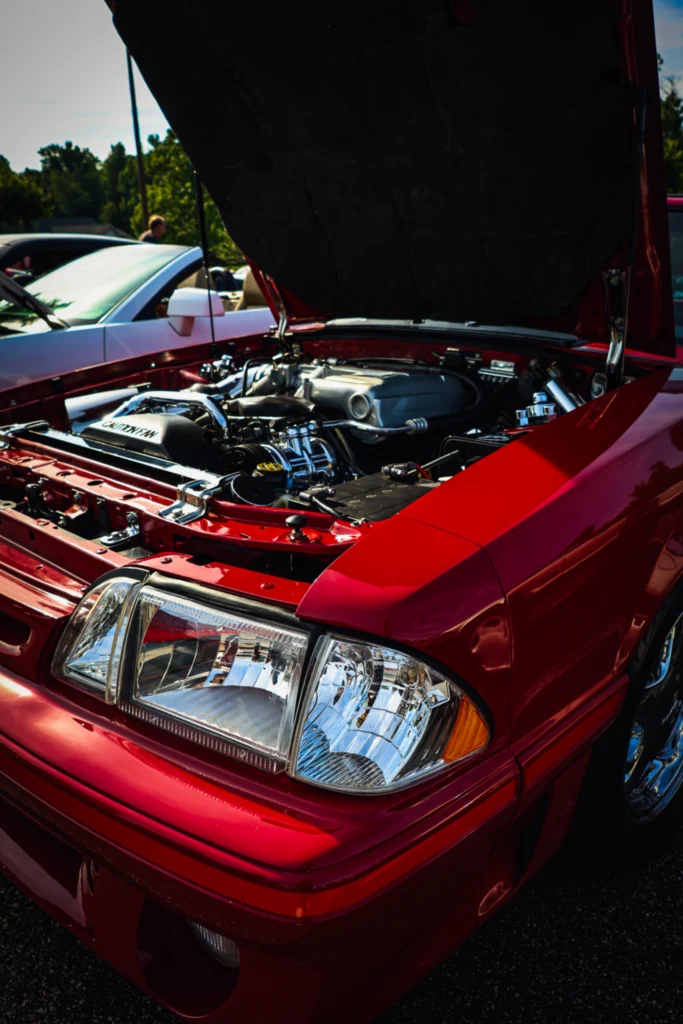 Open hood of a red Mustang truck showing a detailed engine bay at an outdoor car event