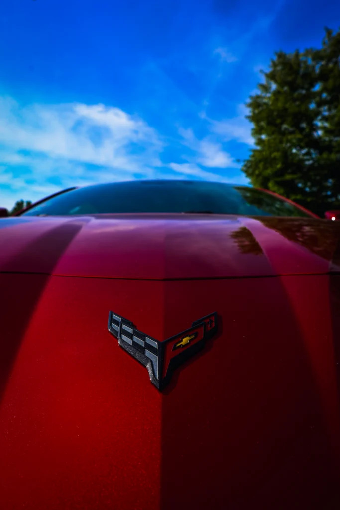 Red Chevrolet Corvette hood with emblem under blue sky and tree in background