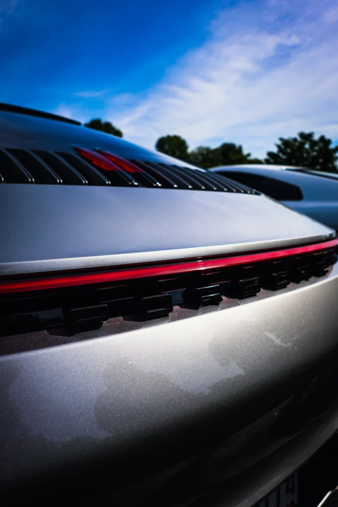 Rear detail of a silver Porsche sports car under a blue sky at an outdoor event.
