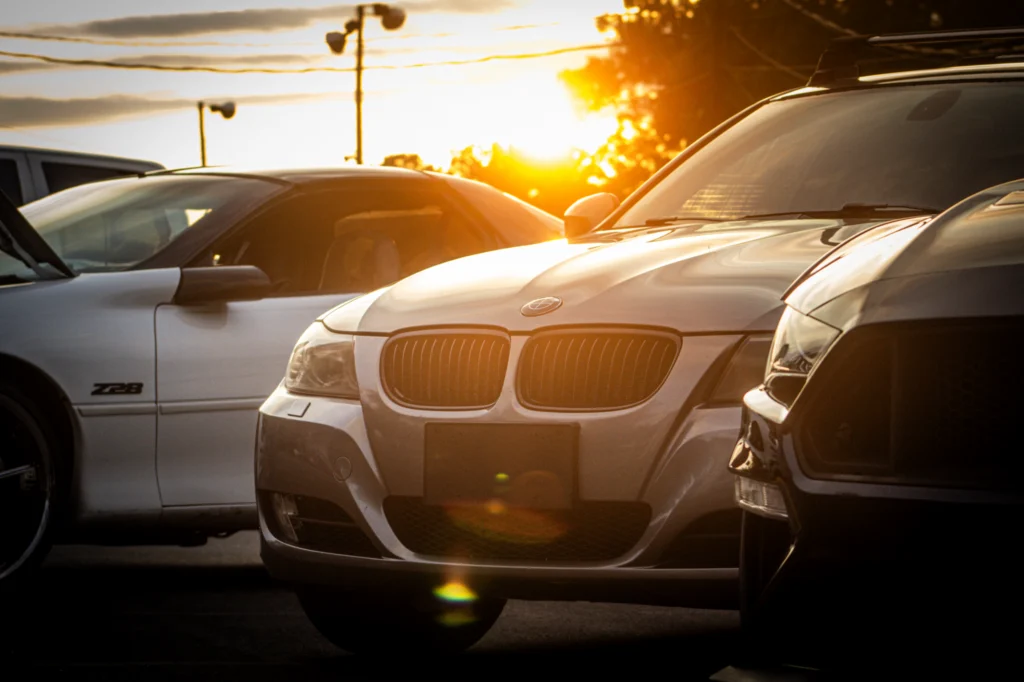White Chevy Camaro Z28 and silver BMW parked side by side at sunset with a black vehicle partially in frame
