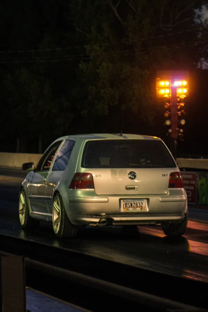 Silver Volkswagen Golf 1.8T parked at night on a drag strip near a lit drag racing Christmas tree