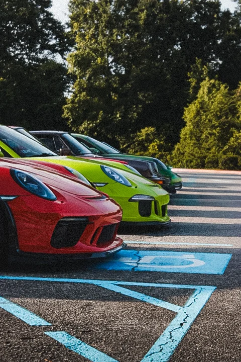 Row of Porsche 911 sports cars in various colors parked next to each other in a lot with trees in the background