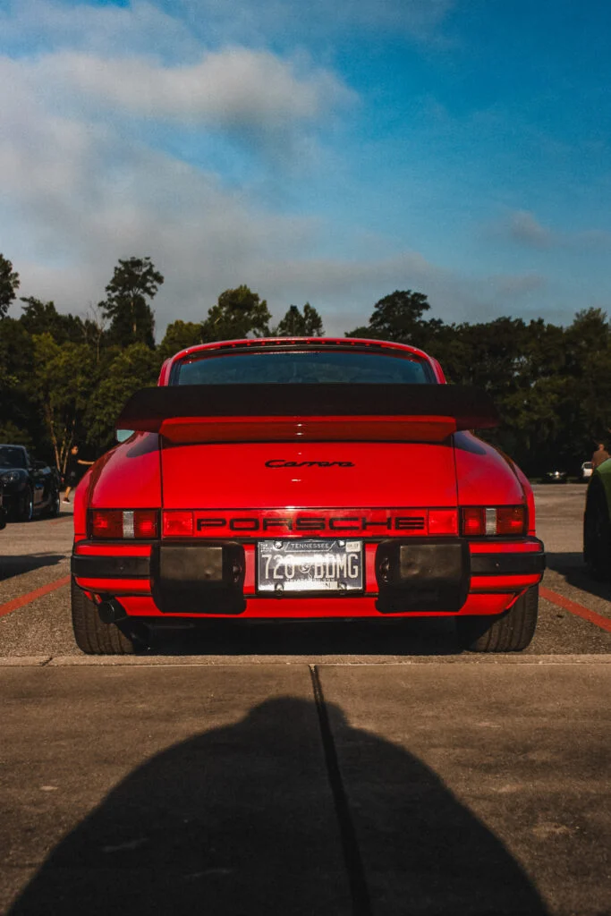 Rear view of a red Porsche Carrera with a black rear spoiler parked outdoors under blue sky