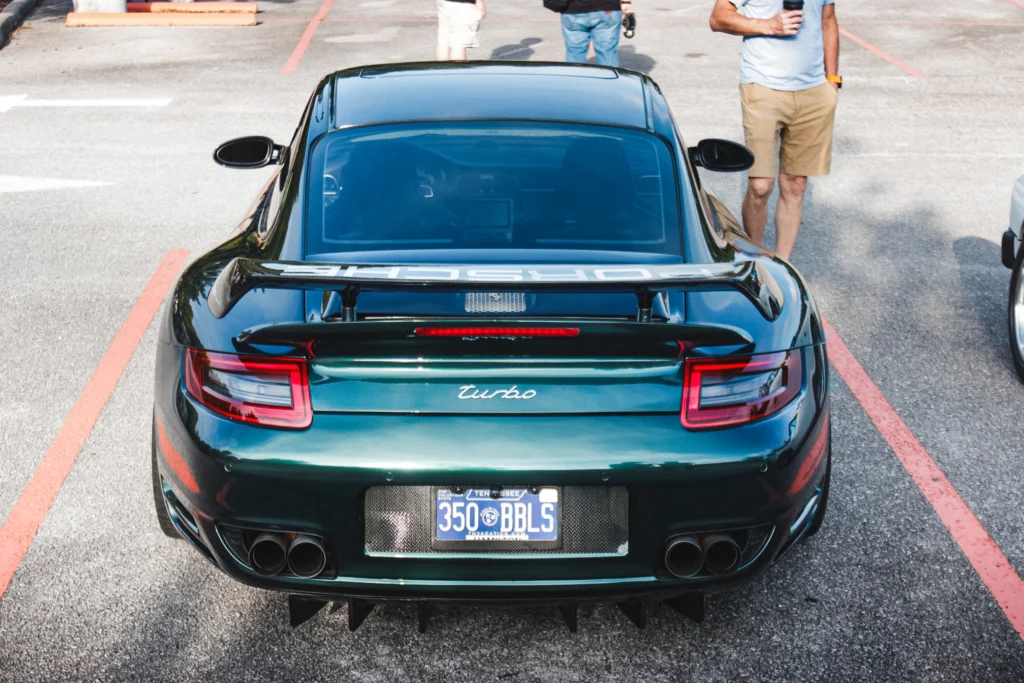 Rear view of a dark green Porsche Turbo with a Tennessee license plate parked in an outdoor lot at a car event.