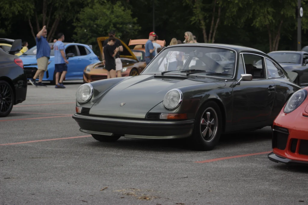Dark gray Porsche 911 parked with other vehicles and people in the background at an outdoor car event