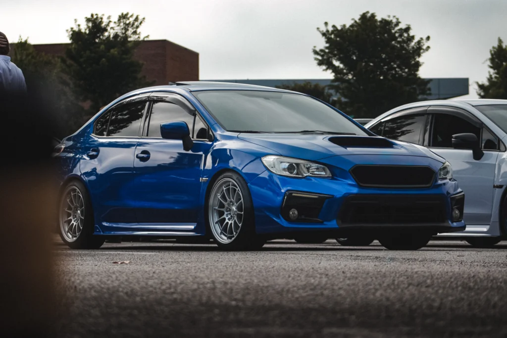 Blue Subaru WRX parked outdoors with trees and another car in the background