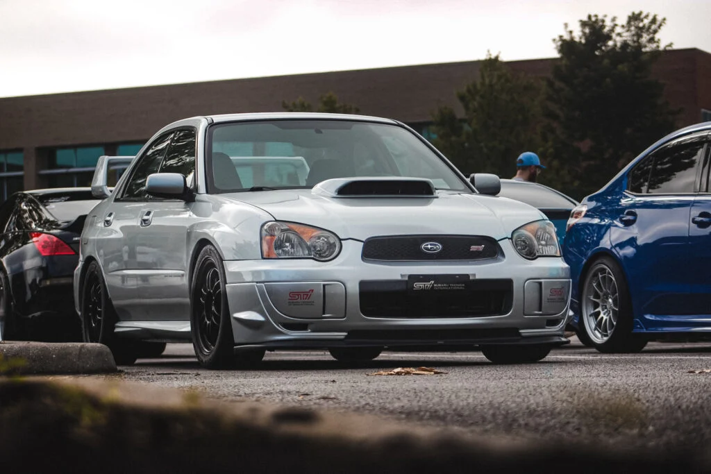 Silver Subaru WRX STI sedan parked outdoors with other vehicles and a person in the background