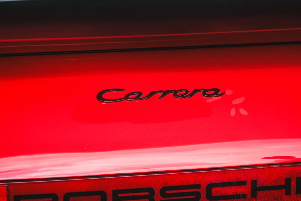 Rear badge and tail light area of a red Porsche Carrera