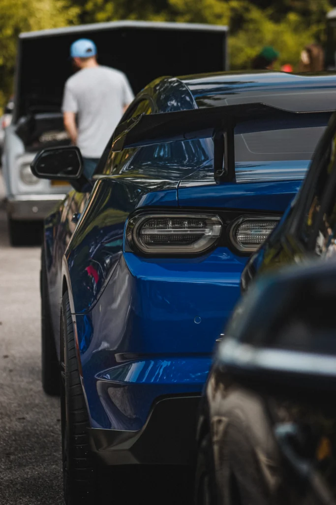 Rear view of a blue Chevrolet Camaro with a large spoiler, parked alongside other cars at an outdoor event
