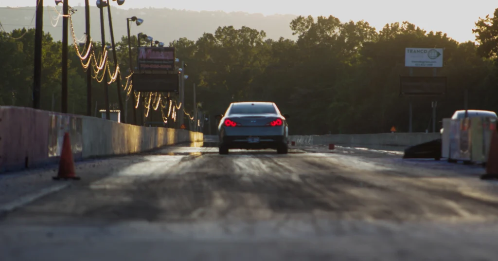 Infiniti G37 with red rear lights illuminated driving on a drag strip at sunset with trees in the background