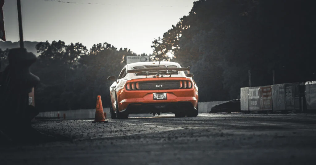 Orange Ford Mustang GT on a race track with trees and barriers in the background