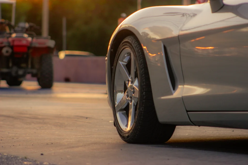 Close-up of a Chevrolet Corvette's front wheel and fender with two ATVs in the background at sunset
