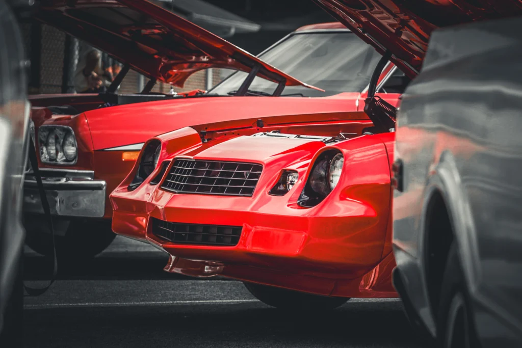 Two red Chevrolet Camaros with open hoods parked side by side at an outdoor car event.
